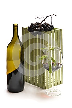 A bottle of wine and bunches of ripe grapes in a glass on a white background