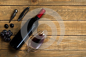 Bottle of wine and corkscrew cup and grapes on wooden background. Top view with copy space
