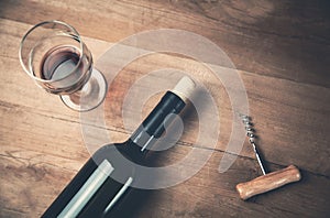 Bottle of wine corkscrew and glass on wood background.
