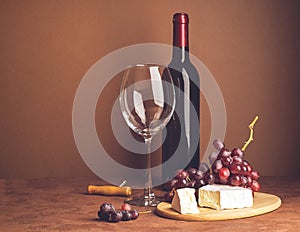 A bottle of wine an empty glass bunch of red grapes a slice of cheese on a dark background. Copy space. Selective focus