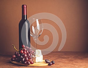 A bottle of wine an empty glass bunch of red grapes a slice of cheese on a dark background. Copy space. Selective focus.