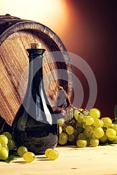 Bottle of wine in front, wine barrel and white grapes.