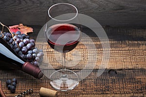 A bottle of wine, a glass, a bunch of grapes and grape leaves on an old wooden table