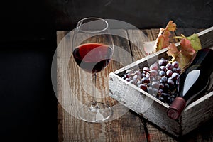 A bottle of wine, a glass, a bunch of grapes and grape leaves on an old wooden table