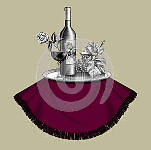 Bottle of wine with a glass, bunch of grapes with leaves, metal tray on a round table and old ribbon banner