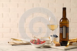 Bottle of wine, glass and delicious snacks on white marble table