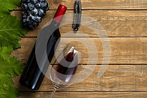 Bottle of wine glass grapes and corkscrew on wooden background. Top view with copy space