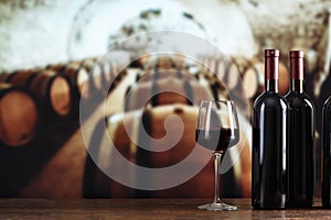 A bottle of wine and glasses with wine on a barrel in a wine cellar