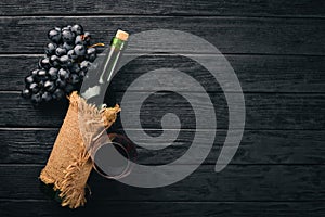 A bottle of wine with glasses and grapes on a black wooden background.