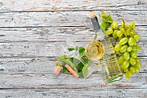 A bottle of wine with glasses and grapes. Leaves of grapes. Top view. On a white wooden background.