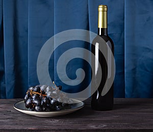 A bottle of wine and grapes on a plate on a fabric wavy background