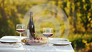 A bottle of wine with snacks is on the table. In the background, blurred outlines of the vineyard. Place for romantic