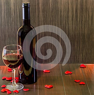 Bottle of wine with transparent glass with red wine, textile red hearts, wood texture background, close up