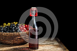 Bottle of wine vinegar and basket with fresh grapes on wooden table against black background.