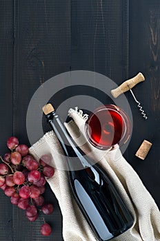 Bottle of wine, wine glass, grapes and corkscrew on dark background
