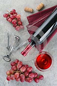 Bottle of wine, wine glass, grapes and corkscrew on gray background