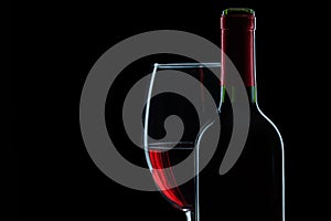 Bottle and wineglass with red wine on black background close up view