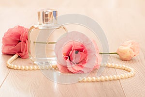 Bottle of woman perfume with beads on a string and flowers on pink background