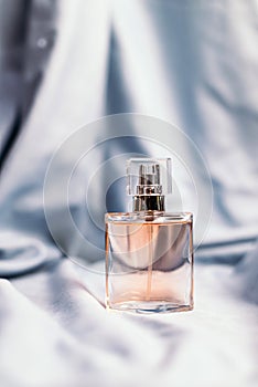 A bottle of women`s fragrant perfume on a silk textured fabric background