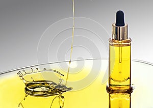 The bottle of yellow moisturizing cosmetic oil on the big oil splash on the gradient grey background