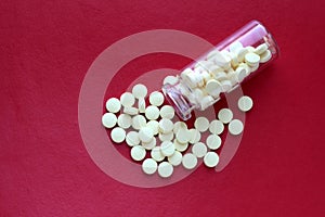 A bottle of yellow pills on a purple background. Scattered vitamins