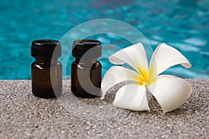 Bottles of aroma essential oil and flower of frangipani on the swimming pool background.