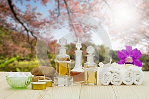 Bottles of aromatic oils with candles, pink orchid, stones and white towel on vintage wooden floor on lake and forest background