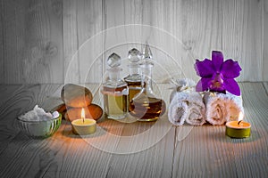 Bottles of aromatic oils with candles, pink orchid, stones and white towel on wooden background with vignette