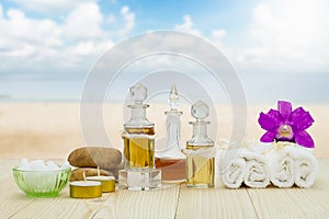 Bottles of aromatic oils with candles, pink orchid, stones and white towel on wooden floor on blurred beach and sky background