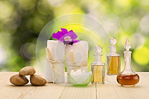 Bottles of aromatic oils with pink orchid, stones and white towel on vintage wooden floor on blurred green bokeh background