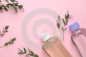 Bottles of baby oils and green leaves on pink background, flat lay. Space for text