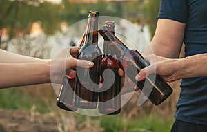 Bottles with beer in the hands of young people in nature. Selective focus.