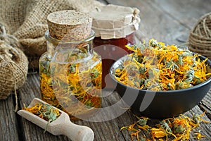 Bottles of calendula infusion, healthy marigold flowers in bowl and calendula salve on wooden table. Herbal medicine