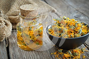 Bottles of calendula infusion, healthy marigold flowers in bowl and canvas sack on background. Herbal medicine