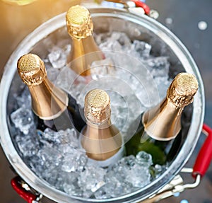 Bottles of champagne in bucket with ice on blurred background, closeup