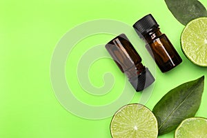 Bottles of citrus essential oil and fresh limes on green background, flat lay. Space for text