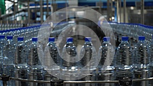 Bottles of clean drinking water are moving on a conveyor belt. Production of mineral water at a food processing plant