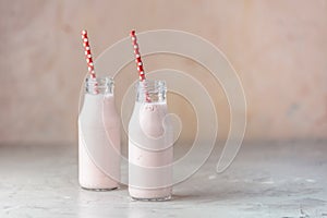 Bottles with delicious strawberry milkshake or smoothie on table and pink background