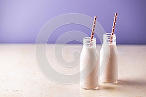 Bottles with delicious strawberry milkshake or smoothie on table and violet background