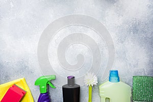 Bottles with detergents, brushes and sponges on concrete background. Colorful cleaning products. Home cleaning concept. Top view,