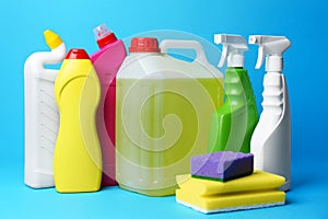 Bottles of detergents and sponges on light blue background. Cleaning supplies