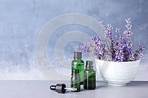 Bottles of essential oil and bowl with lavender flowers on stone table against blue background