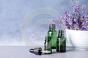 Bottles of essential oil and bowl with lavender flowers on stone table against blue background
