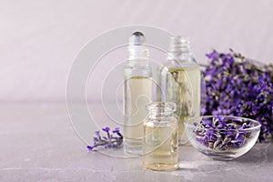 Bottles of essential oil and bowl with lavender flowers on stone table against light background