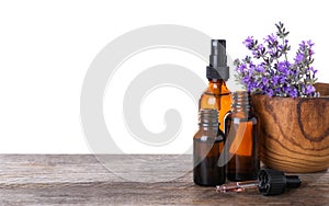 Bottles of essential oil and bowl  lavender flowers on wooden table against white background