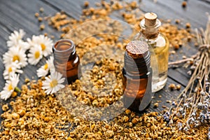 Bottles of essential oil with dried flowers on wooden table