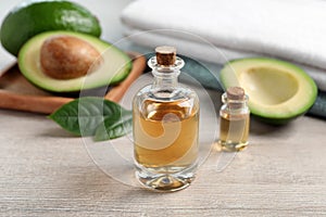 Bottles of essential oil, fresh avocado and towels on light wooden table