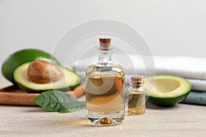 Bottles of essential oil, fresh avocado and towels on light wooden table