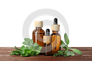 Bottles of essential oil and fresh herbs on wooden table against white background