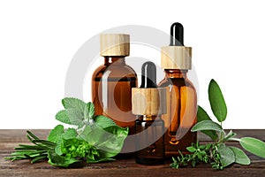 Bottles of essential oil and fresh herbs on wooden table against white background